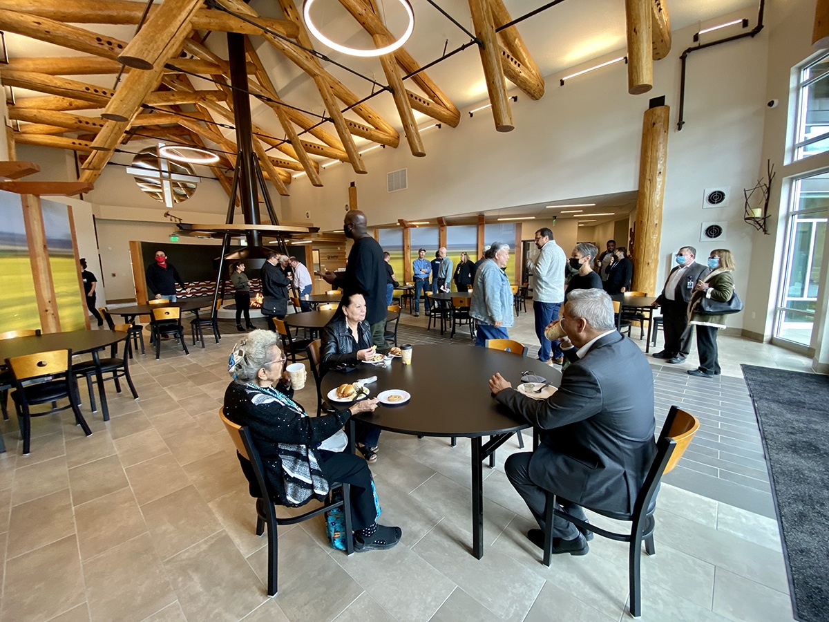 People are seated around tables in the dining room during the Grand Opening celebration with some people walking through the room