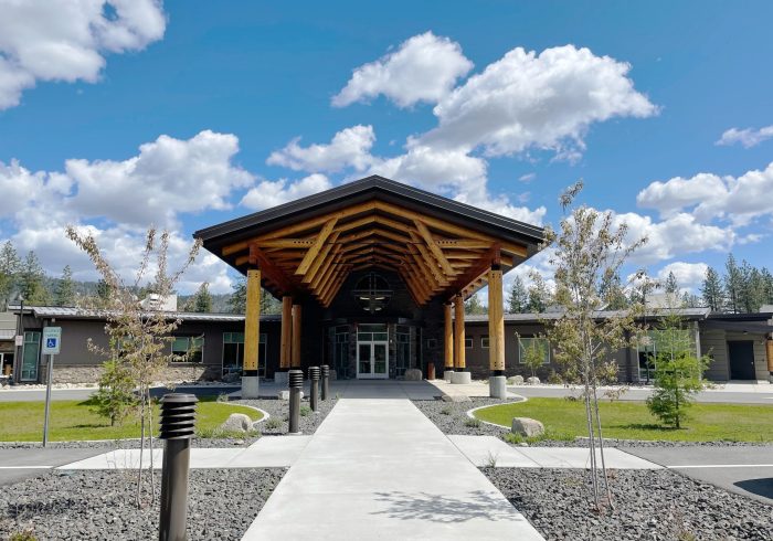 View of main entrance from sidewalk shows large vaulted portico featuring logs